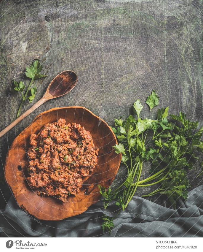 Lebensmittel Hintergrund mit Fleisch Füllung auf dunklen Tisch mit Kräutern, Holzkochlöffel und Geschirrtuch. Kochen mit Hackfleisch und Petersilie. Draufsicht mit Kopierbereich.