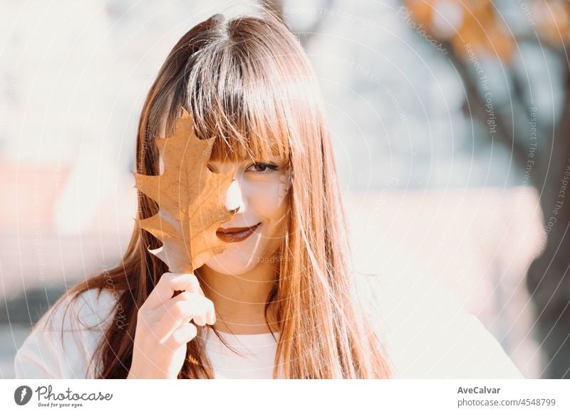 Glückliche hübsche junge rothaarige Frau mit einem süßen Lächeln in einem weißen T-Shirt mit einem Ahornblatt in den Händen. Goldenes Laub. Herbstliche Konzept, lächelnd glücklich, saisonale Moment. Nahaufnahme Porträt