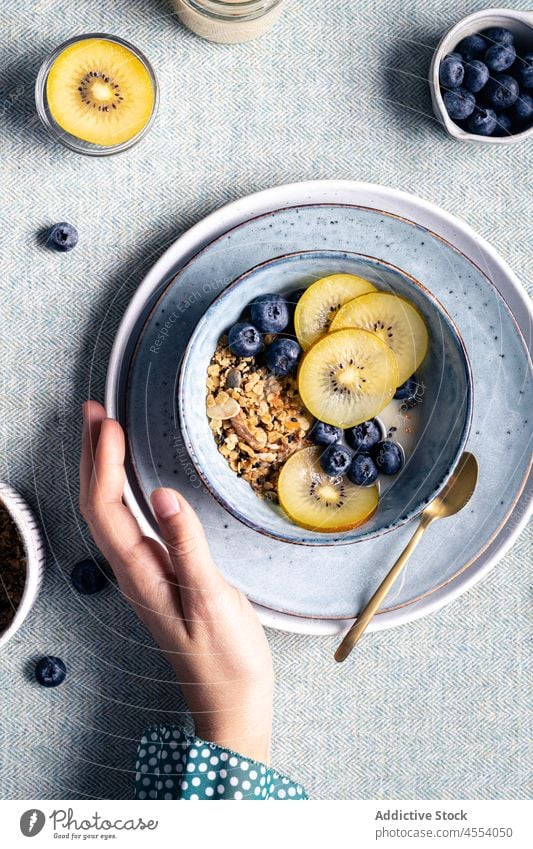 Frau mit einer Schüssel Müsli zum Frühstück Kiwi Schalen & Schüsseln Morgen Blaubeeren gesunde Ernährung Mahlzeit selbstgemacht lecker Frucht Tisch Beeren