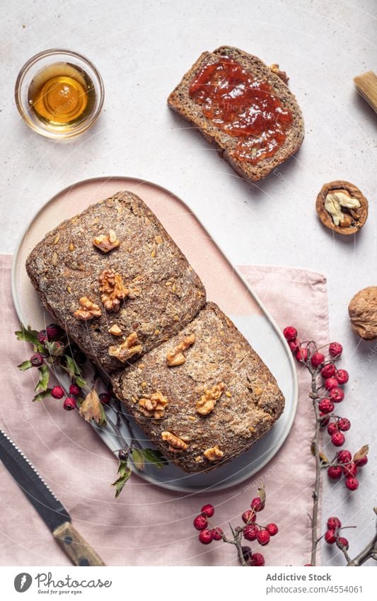 Laib Brot mit Marmelade und Honig Korn Brotlaib geschnitten gebacken selbstgemacht Walnussholz Zusammensetzung Messer Samen Spielfigur Glas süß Lebensmittel