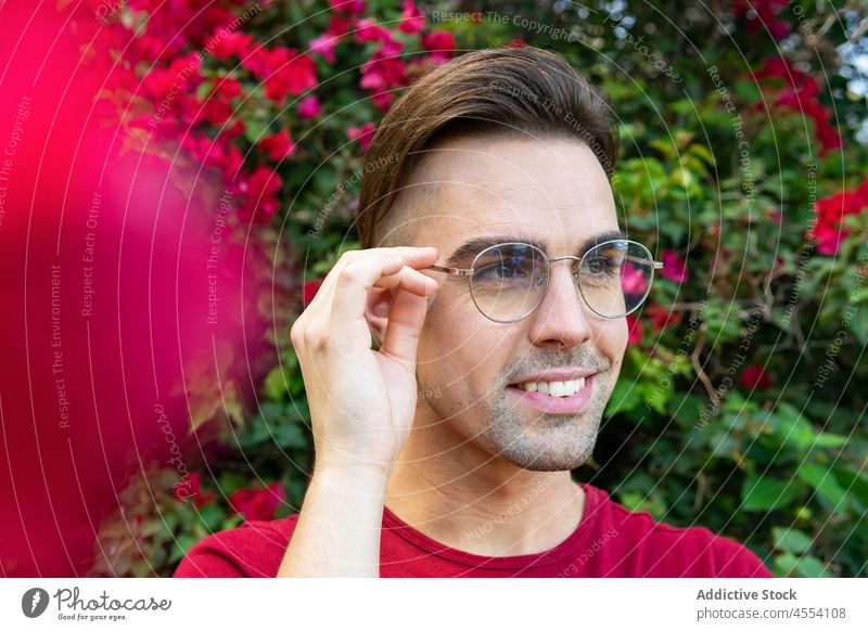 Lächelnder Mann vor blühendem Busch im Garten positiv Porträt Blütezeit Strauch Blume Brille Persönlichkeit Glee genießen männlich Zahnfarbenes Lächeln froh