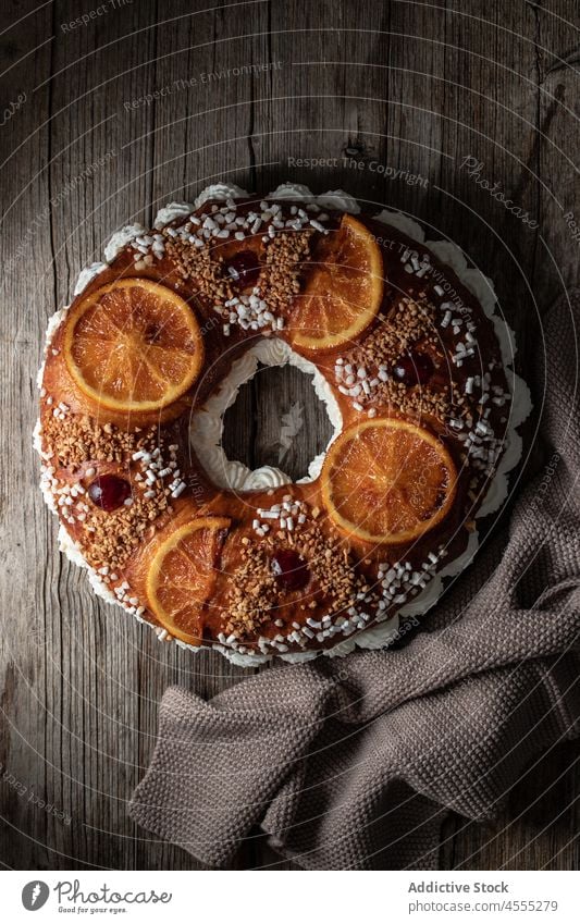 Königskuchen auf Holztisch süß Kuchen Dessert Lebensmittel Roscon de reyes Sahne lecker geschmackvoll orange Spanisch Tisch bestäuben Handtuch Zitrusfrüchte