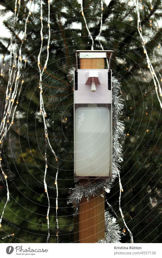 desinfektionsmittel spender auf dem weihnachtsmarkt weihnachtsdeko weihnachtsbaum lichterkette tannengrün weihnachtszeit draußen öffentlich hände desinfizieren