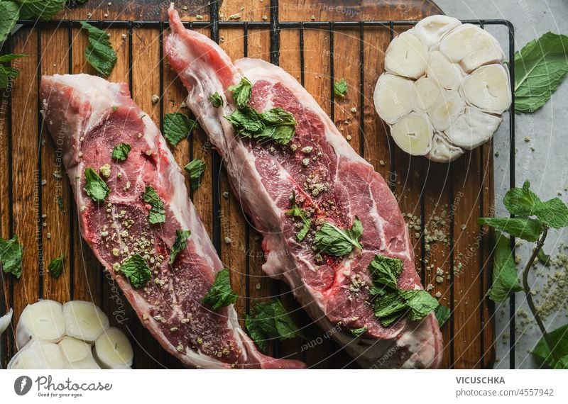 Nahaufnahme von rohen Fleischstücken mit Minze, Gewürzen und Knoblauch auf einem hölzernen Schneidebrett. Frisches Steak zu Hause mit schmackhaften Zutaten zubereiten. BBQ-Zubereitung. Ansicht von oben.