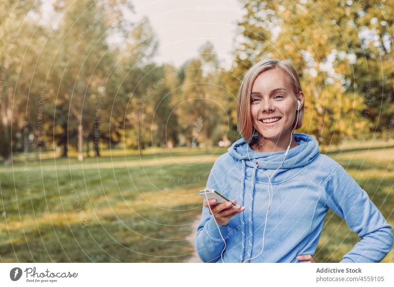 Junge Frau hört Musik über Kopfhörer auf einem Smartphone zuhören Apparatur Porträt Park Gerät Kapuzenpulli Melodie Mobile Klang Audio Gesang Telefon benutzend