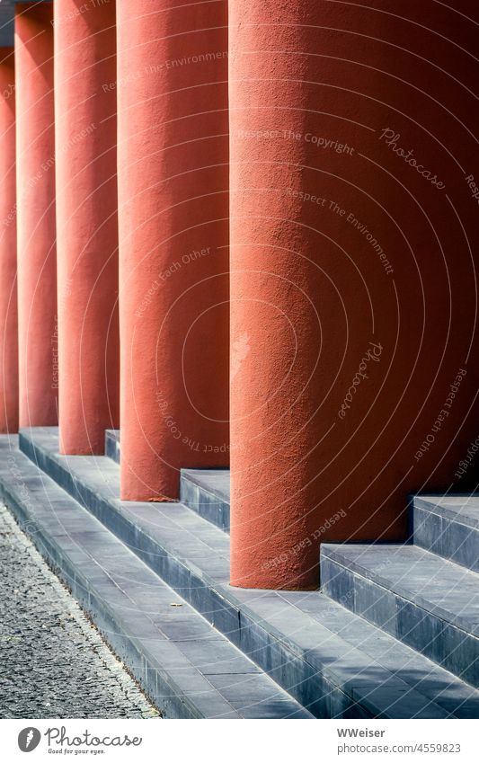 Dicke orangerote Säulen tragen das Vordach des Gebäudes, dazwischen liegen Stufen abstrakt geometrisch urban Architektur Design Fassade Außenseite Struktur