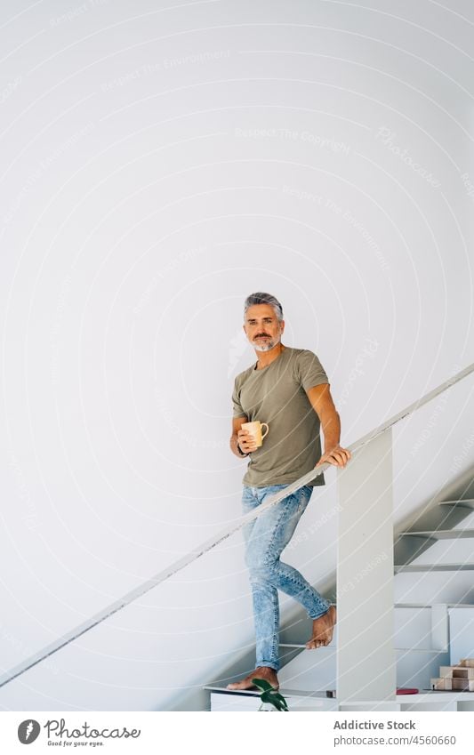 Älterer Mann auf Stufen mit Teetasse Treppenhaus Loft Schritt Innenbereich Tasse trinken Getränk männlich Treppengeländer Heißgetränk gealtert Senior Kaffee