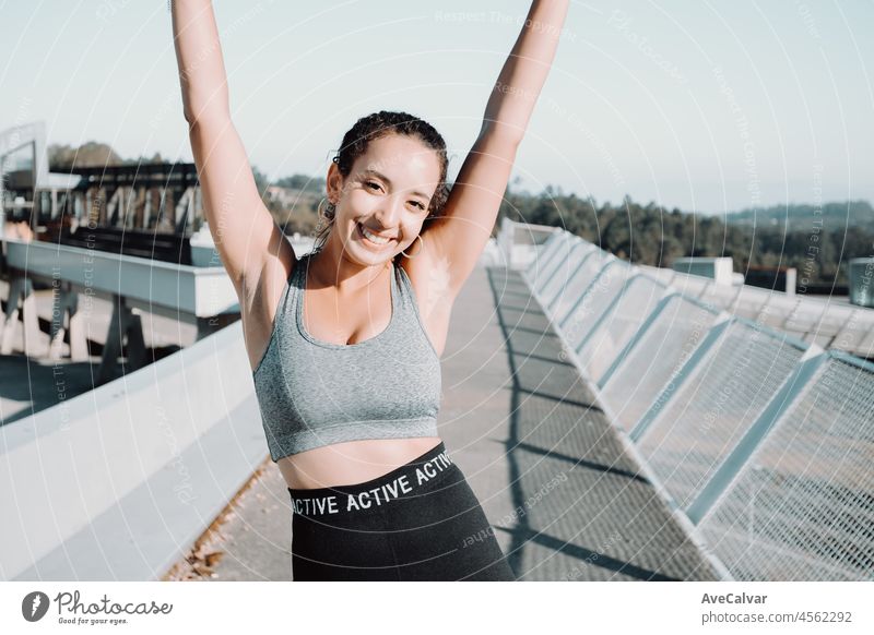 Schönes Mädchen Athleten, afrikanische gebräunte Haut. Fröhliches Feiern nach urbanem Training. Winken mit den Armen und lächelnd in die Kamera. Sicheres Training an der frischen Luft. Leggings Kleidung und Top. Kopieren Raum Bild. Schönheit