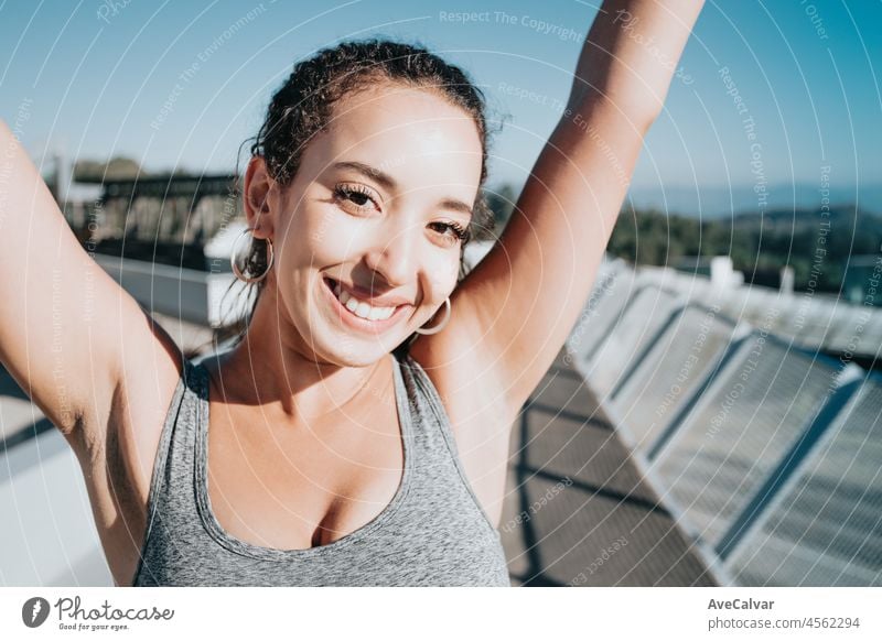 Schönes Mädchen Athleten, afrikanische gebräunte Haut. Fröhliches Feiern nach urbanem Training. Winken mit den Armen und lächelnd in die Kamera. Sicheres Training an der frischen Luft. Leggings Kleidung und Top. Kopieren Raum Bild. Schönheit