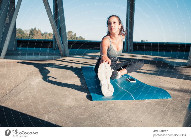 Schönes Mädchen Athleten, afrikanische gebräunte Haut. Lächelt in die Kamera, während sie ihre Muskeln aufwärmt, bevor sie urbanes Yogatraining macht. Musik beim Training. Sitzender Boden Kopie Raum