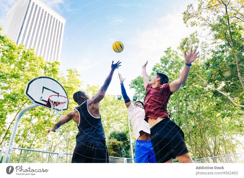 Eine Gruppe von Freunden springt und wirft den Ball hoch Männer werfen Basketball spielen springen Spieler Straße Sport positiv Mann multiethnisch heiter Glück