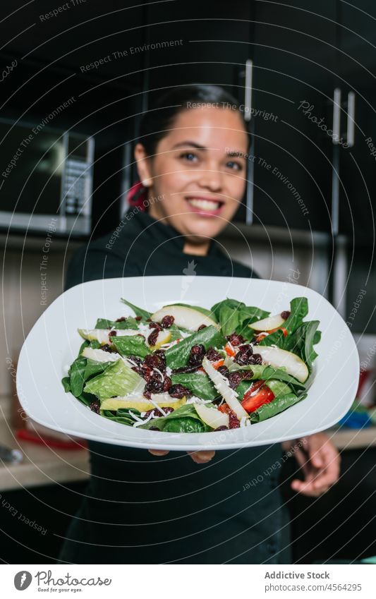 Fröhliche Köchin demonstriert Gericht mit Birnen und Salatmais Frau Küchenchef Gemüse Salatbeilage lecker geschmackvoll Speise Teller Koch frisch Uniform