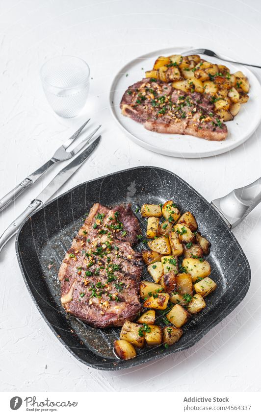 Leckeres Rindfleisch mit Kartoffeln auf dem Tisch hacken Fleisch gebraten Speise Mahlzeit gehackter Knoblauch Petersilie Bratpfanne dienen Glas Wasser Getränk