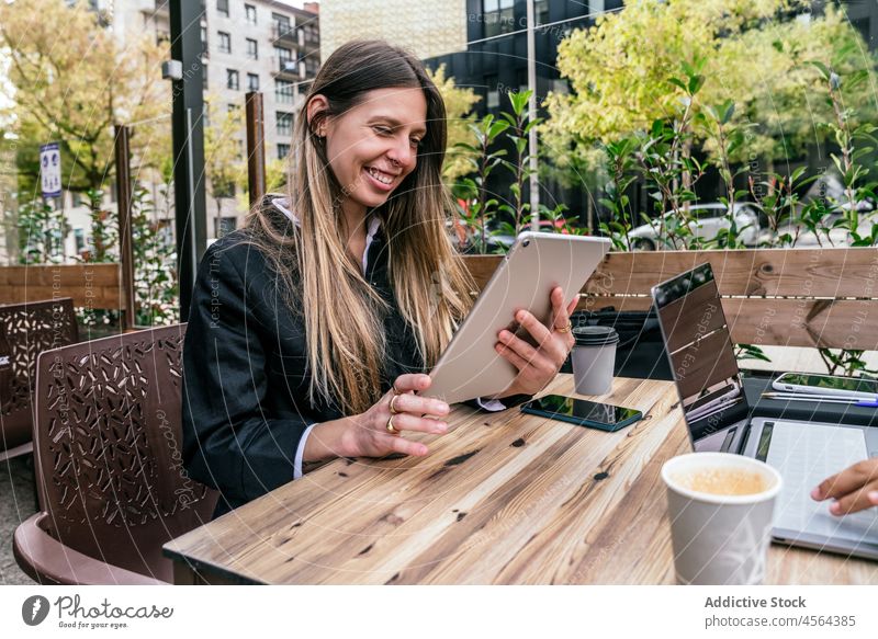 Fröhliche Geschäftsfrau in der Nähe eines gesichtslosen Mitarbeiters am Tisch mit Gadgets Geschäftsfrauen Café Terrasse Tablette Laptop online Browsen