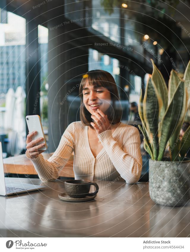 Gut gelaunte Frau mit einer Tasse Kaffee und einem Mobiltelefon Laptop benutzend Browsen Gerät Anschluss abgelegen Geschäftsfrau freiberuflich Telefon trinken