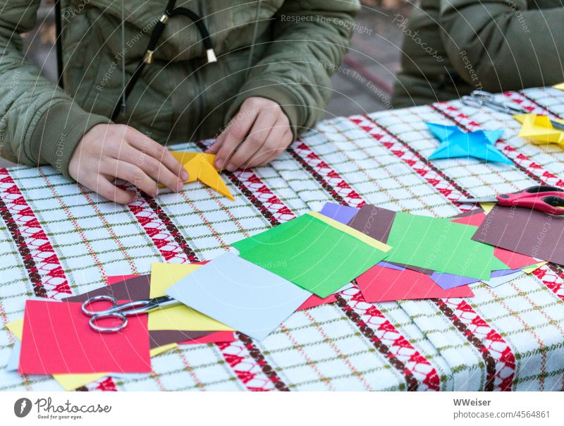 Auf dem Weihnachtsmarkt basteln Kinder und Erwachsene gemeinsam bunte Sterne aus Papier Bastelstand Advent kalt Winter Vorfreude Geschenke selbstgemacht Hände