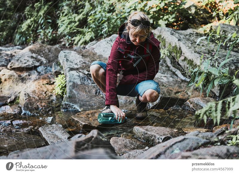 Frau, die beim Trekking in den Bergen reines Wasser aus einem Bergbach in eine Flasche füllt Abenteuer Ausflug reisen wandern durstig strömen Urlaub Reise