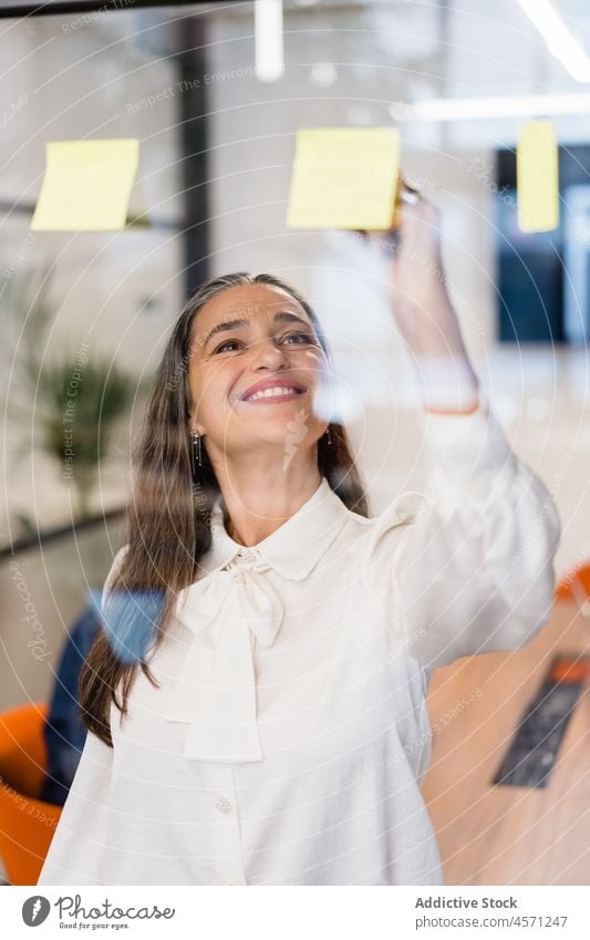 Durch das Glas einer Geschäftsfrau, die auf Notizzetteln schreibt Frau Haftnotiz schreiben zur Kenntnis nehmen Glaswand Arbeit Büro Arbeiter Unternehmen