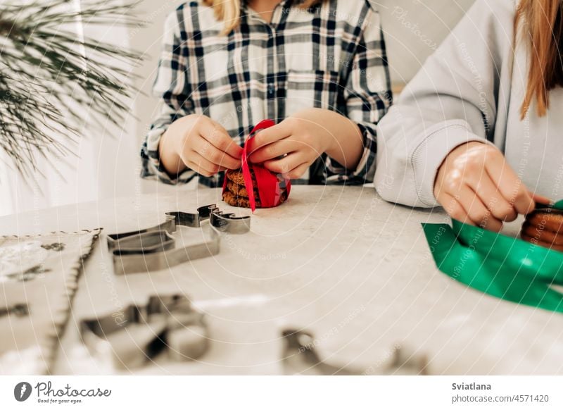 Nahaufnahme der Hände des Mädchens mit einer roten Schleife Weihnachtsplätzchen gebunden. Vorbereitung für die Feiertage, Geschenke, süße Leckereien Weihnachten