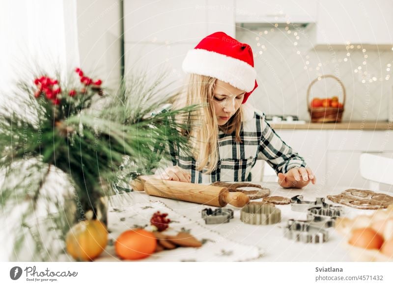 Ein Mädchen mit einer roten Weihnachtsmütze stellt in der Küche Lebkuchenteig her. Weihnachtstradition, Weihnachtsatmosphäre, Vorbereitung auf die Feiertage