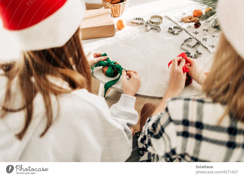 Zwei Mädchen verzieren Plätzchen mit leuchtend roten und grünen Bändern und bereiten süße Leckereien für Gäste an Weihnachten oder Silvester vor Geschenk neu