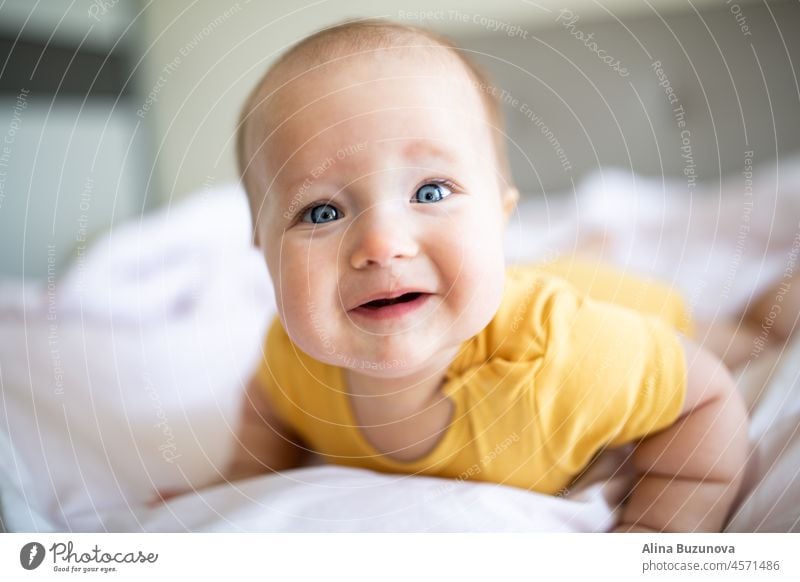 Kaukasische blonde Baby sieben Monate alt auf dem Bett zu Hause liegen. Kind trägt niedliche Kleidung gelbe Farbe neugeboren Säugling lichtvoll ultimativ grau