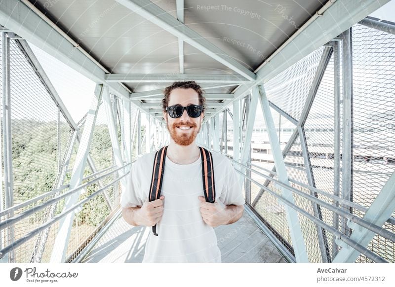 Porträt eines jungen Mannes auf dem Flughafen oder Busbahnhof, Gepäck, Taschen und Koffer. Lächelnder Hipster-Reisender mit Sonnenbrille, Kopierraum, sonniger Tag