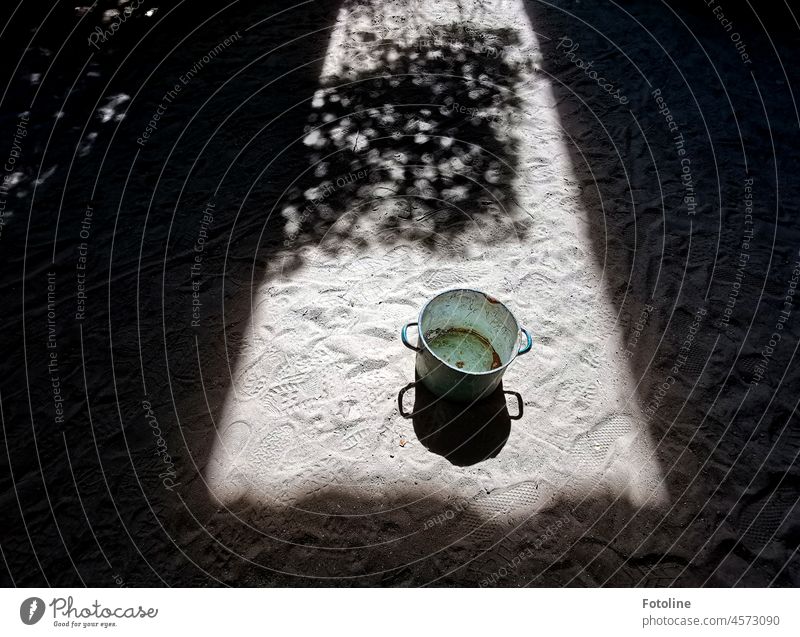 Auf dem Boden im Sand eines alten Lost Places steht ein Lost Topf im Sonnenlicht, umrahmt von dunklen Schatten. rostig Metall Rost Außenaufnahme Farbfoto