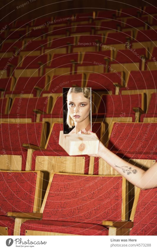 Ein wunderschönes Mädchen schaut in einen Spiegel. Ihre roten Lippen, ihr Make-up und ihre Frisur sehen prächtig aus. Der Hintergrund eines alten Theaters vermittelt ein interessantes Gefühl, dass es in dieser Geschichte noch etwas zu enthüllen gibt.