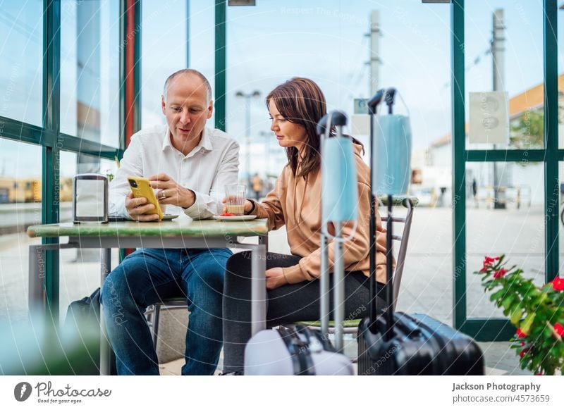 Ein paar Reisende, die Kaffee trinken und etwas am Telefon überprüfen. Das Gepäck mit Masken im Vordergrund. Mundschutz reisen Paar Café Mann blau Schutz