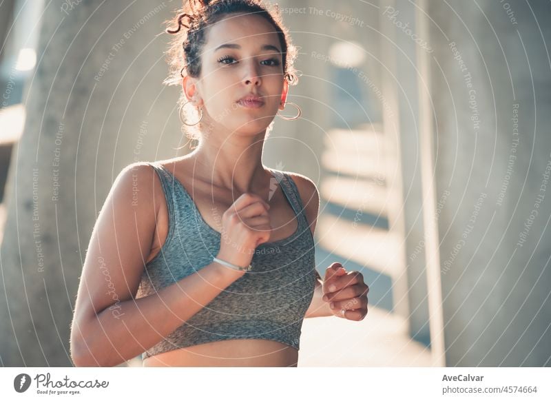 Afroamerikanische junge sportliche Frau, lockige Frisur, läuft im Freien in der Stadt, Korridor Urban Sport in der Stadt. Sonnenuntergang Zeit mit Schatten. Serious Frau konzentriert sich in den Wettbewerb Zug.