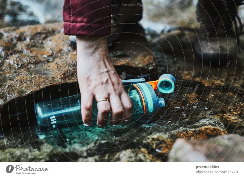 Frau, die beim Trekking in den Bergen reines Wasser aus einem Bergbach in eine Flasche füllt Abenteuer Ausflug reisen wandern durstig strömen Urlaub Reise