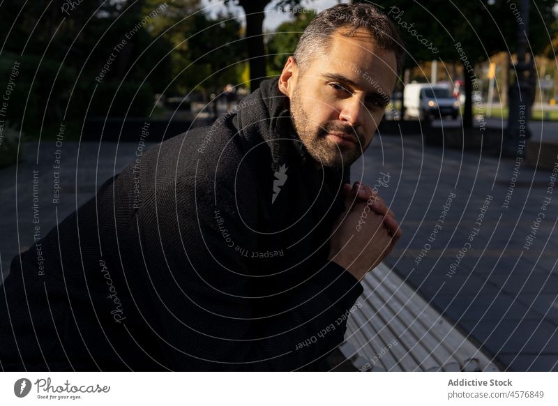 Bärtiger Mann im Mantel steht auf der Straße und schaut in die Kamera Bank Windstille ernst urban Vollbart Vorschein Individualität männlich besinnlich