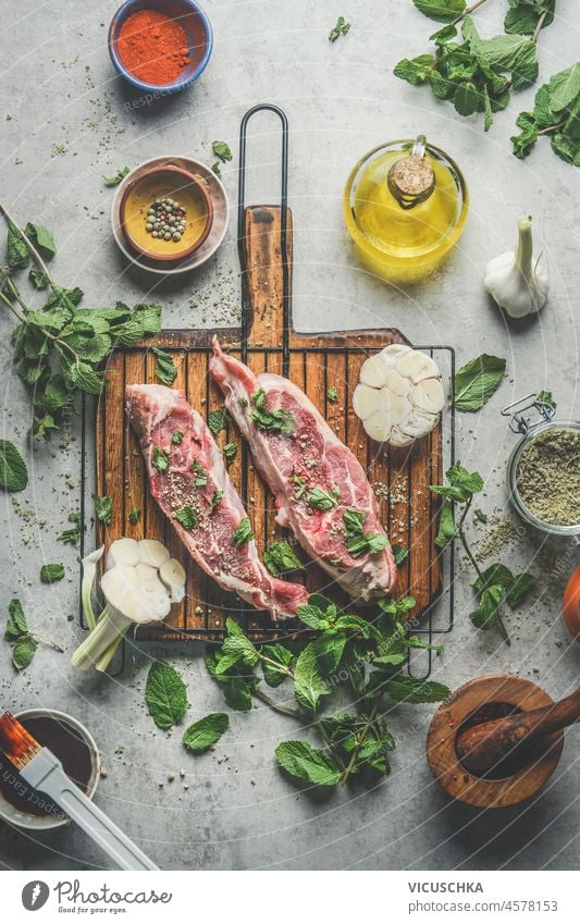 Rohes Fleisch mit Zutaten auf hölzernen Schneidebrett am Küchentisch Hintergrund mit frischen Zutaten Kochen: Olivenöl, Knoblauch, Kräuter und Gewürze. Ansicht von oben.