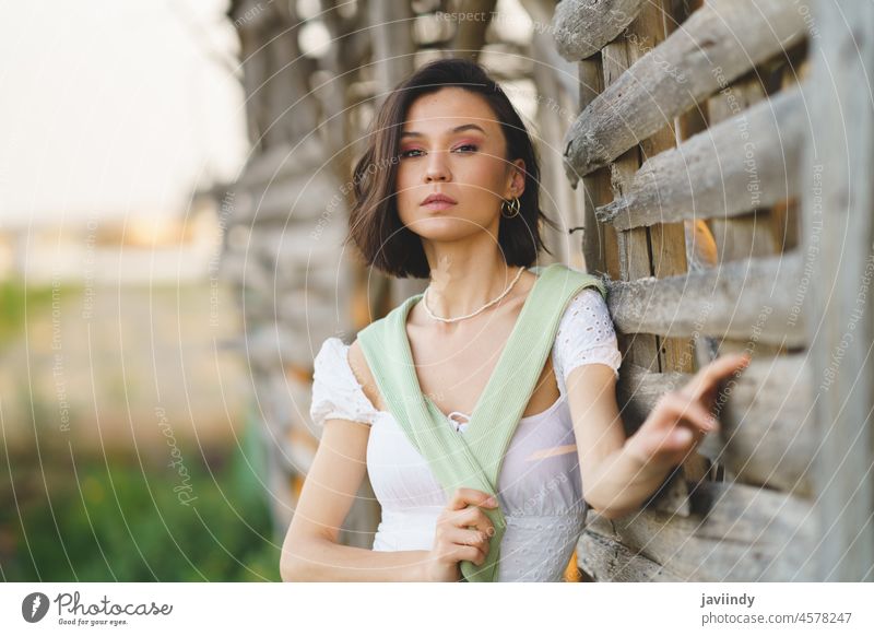 Asiatische Frau in weißem Kleid und grünen Gummistiefeln, die in der Nähe eines Tabaktrockenschuppens posiert. Landschaft Mädchen hübsch Menschen Natur Mode