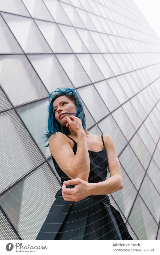 Frau mit blauem Haar steht an der Wand eines modernen Gebäudes Vorschein Zeitgenosse Porträt urban Wolkenkratzer trendy Straße Großstadt Outfit Stil Struktur