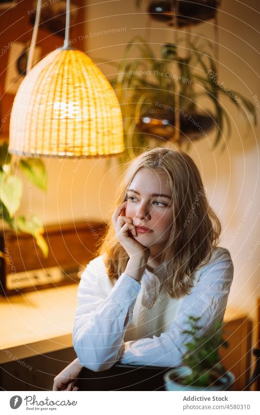 Junges Mädchen sitzt am Schreibtisch unter einem beleuchteten Kronleuchter Frau Lampe Raum Licht heimwärts Bluse leuchten hängen Blume Design Pflanze sitzen