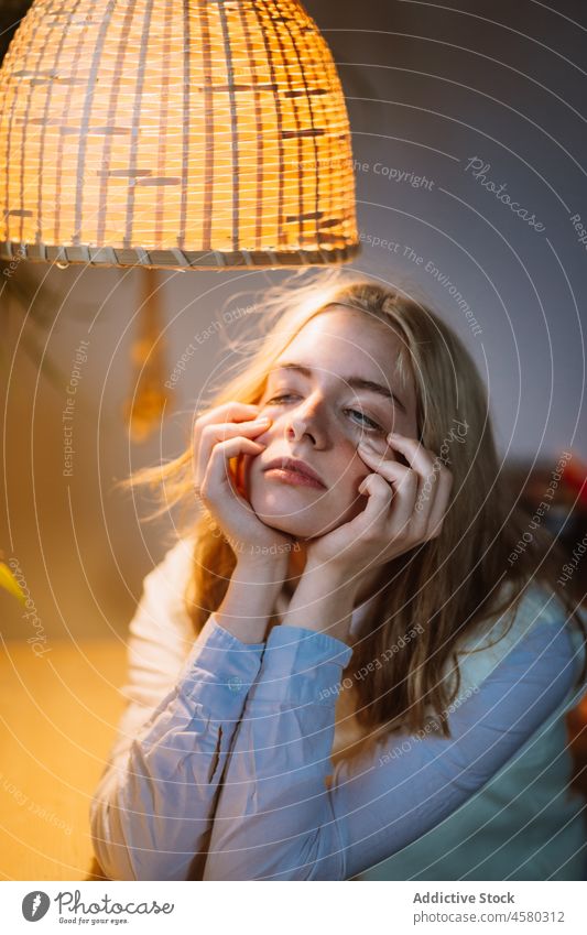 Junges Mädchen sitzt am Schreibtisch unter einem beleuchteten Kronleuchter Frau Lampe Raum Licht heimwärts Bluse leuchten hängen Blume Design Pflanze sitzen