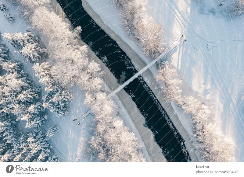 Drone shot frozing kleinen Fluss, Hängebrücke Vogelschau Winterlandschaft Kettenbrücke Ansicht Eis Wald Einfrieren Schnee bedeckt Suspension Brücke sonnig Tag