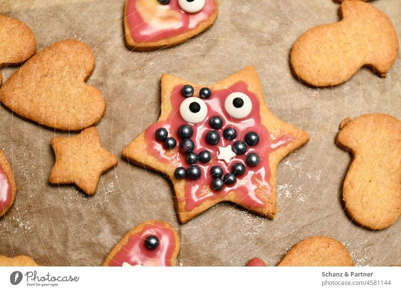 Sternförmiges Weihnachtsplätzchen mit Augen und Zuckerguss Sternsternförmig Plätzchenteig ausstechen Tannenbaum Weihnachtszeit Löffel Gesicht Hand Backpapier