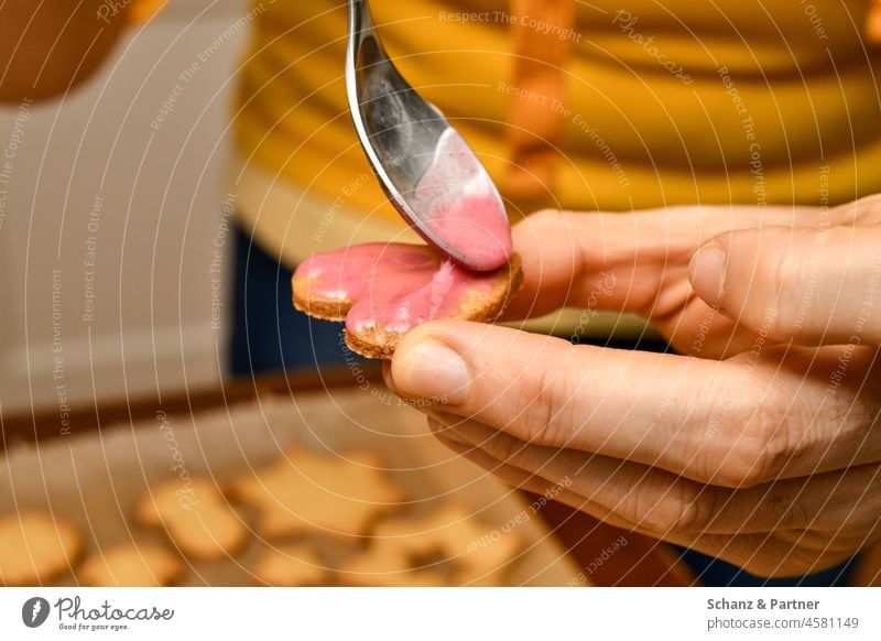 Herzförmiges Plätzchen wird mit Zuckerguss bestrichen rosa Plätzchenteig ausstechen Stern Tannenbaum Weihnachtszeit Löffel Hand Backpapier Teig Finger