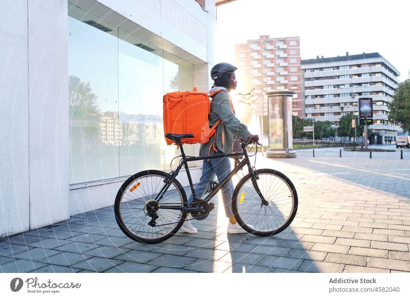 Schwarze Lieferfrau zu Fuß mit Fahrrad Frau Versand Rucksack App Dienst Smartphone Orden Straße Reiter Mitfahrgelegenheit Fahrbahn Arbeit Thermo Gebäude