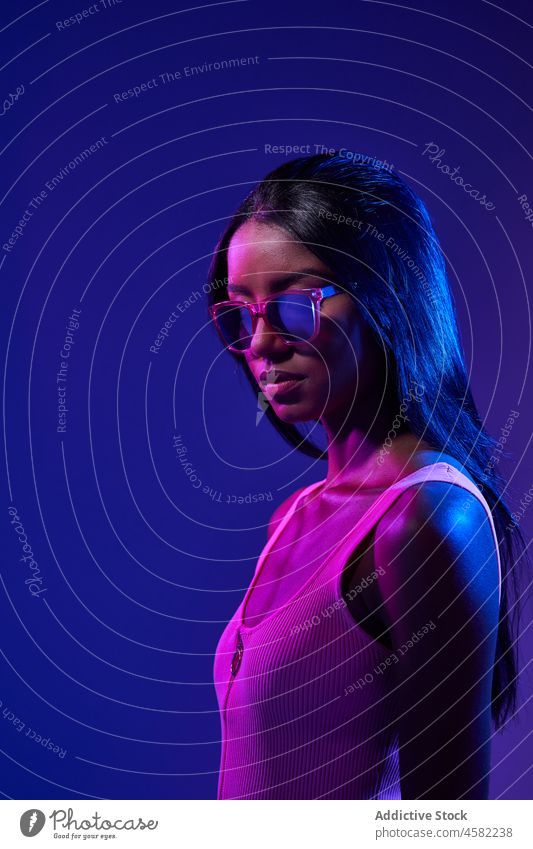 Stilvolle brasilianische Frau im Studio mit Neonlicht Sonnenbrille Accessoire cool trendy Atelier fluoreszierend ultraviolett modern Mode Porträt Licht