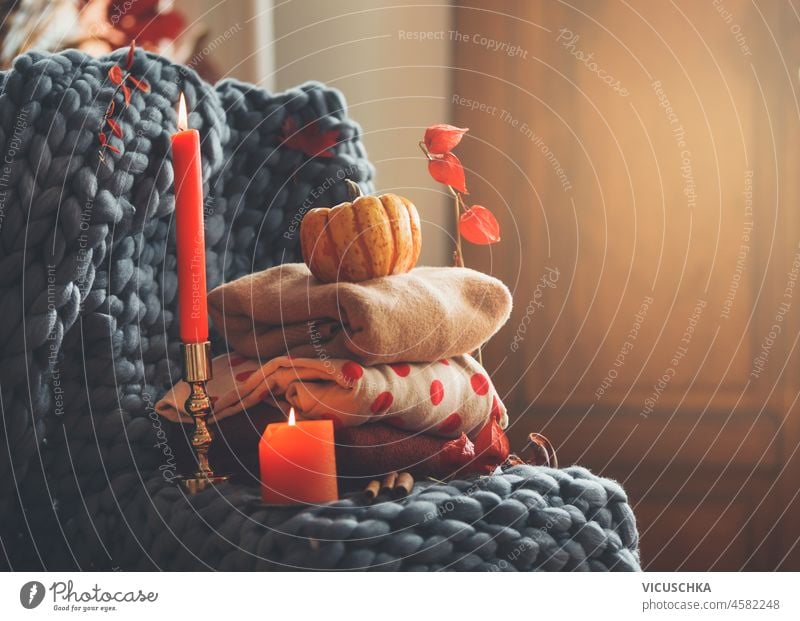 Gemütliches Herbststillleben mit Strickpullovern, Kerzen, grauer Wolldecke, Kerzen und Herbstblättern im Hintergrund. Warme Kleidung für die Herbstzeit. Vorderansicht.