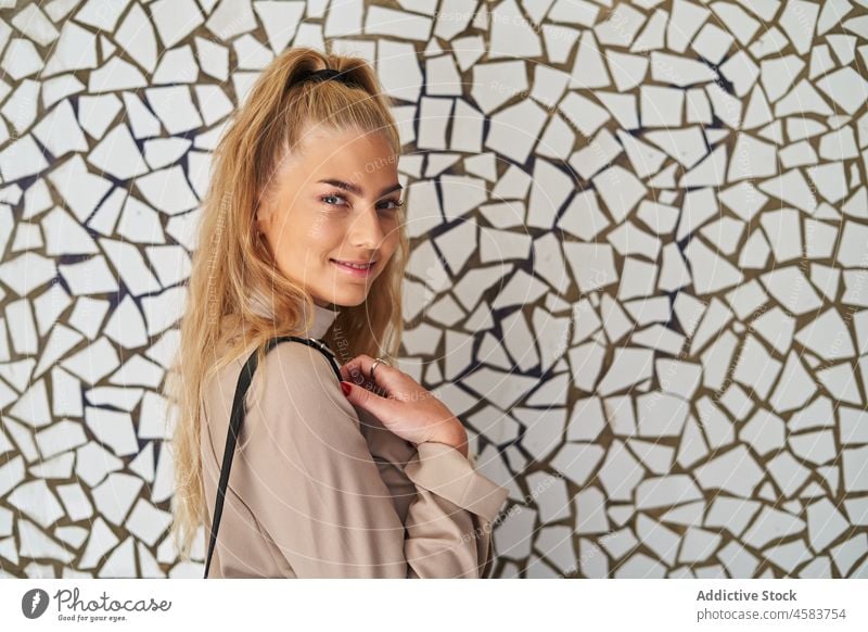 Junge Frau mit Rucksack an Mosaikwand stehend trendy urban Wand Straße Spaziergang Outfit Großstadt blond Leder lässig Windstille tagsüber Sonnenlicht Weg