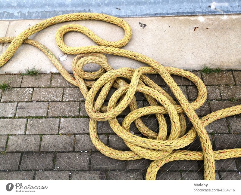 Gelb schimmerndes Schiffstau auf grauem Pflasterstein an einer Anlegestelle im Hafen von Norddeich bei Norden in Ostfriesland in Niedersachsen Seil Tau