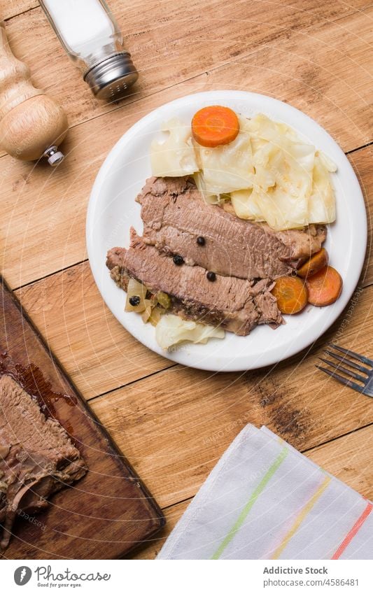 Leckeres in Scheiben geschnittenes Corned Beef mit Kohl und Karottenstückchen Rindfleisch Fleisch Kohlgewächse Möhre dienen hölzern Tisch Teller appetitlich