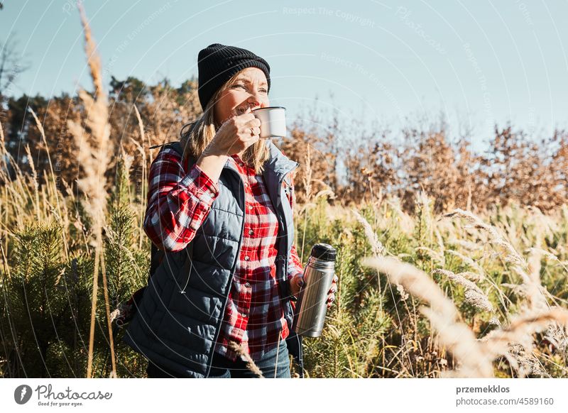 Frau macht Pause und entspannt sich mit einer Tasse Kaffee während eines Sommerausflugs. Frau steht auf dem Weg und schaut weg. Frau mit Rucksack Wandern durch hohes Gras entlang Weg in den Bergen