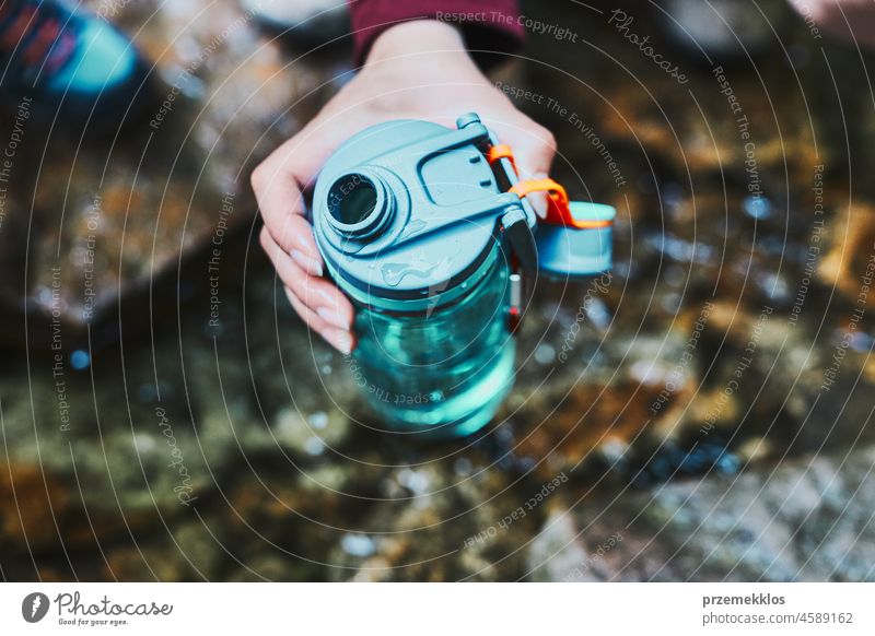 Frau, die beim Trekking in den Bergen reines Wasser aus einem Bergbach in eine Flasche füllt Abenteuer Ausflug reisen wandern durstig strömen Urlaub Reise