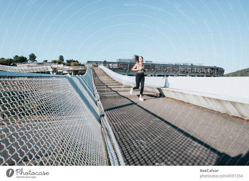 Selbstbewusste junge, fitte afrikanische Sportlerin beim Laufen, während sie mit dem Smartphone draußen in der Stadt Musik hört. Neues Jahr, neue Aktivitäten, neues Leben. Sportlicher Lebensstil. Neue Gewohnheiten.